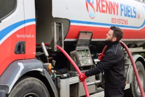 A fuel delivery truck branded "KENNY FUELS.ie" with hoses and a control panel in use for fuel refueling or delivery. A person wearing red gloves manages a hose, emphasizing operational detail.