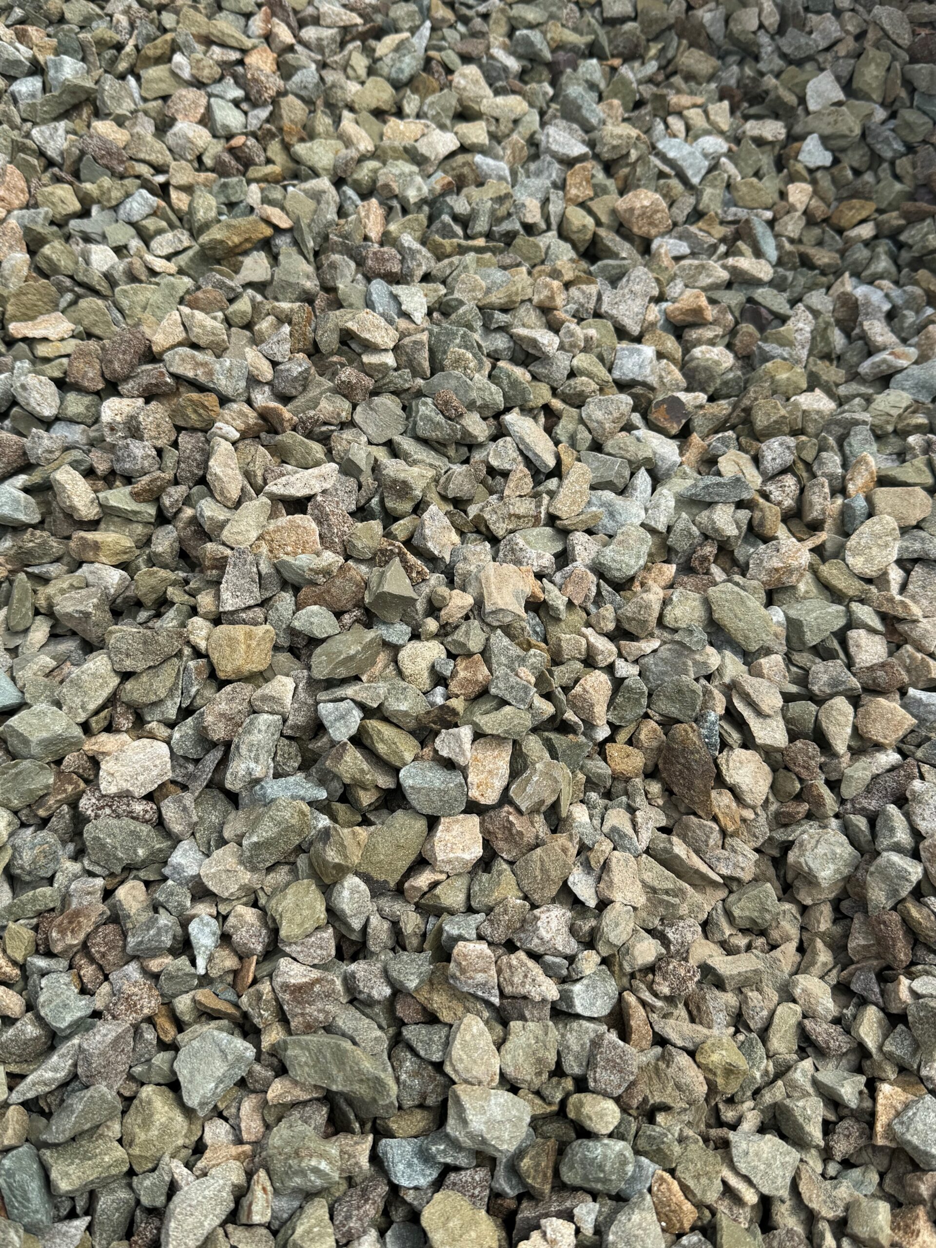 The image shows a large collection of gold stones, approximately 14mm in size. The gravel consists of variously sized and shaped stones, predominantly in shades of gray, brown, and green. They may be used for construction, landscaping, or as a base material for paving. The texture and color variations among the stones are notable, providing a natural and rugged appearance