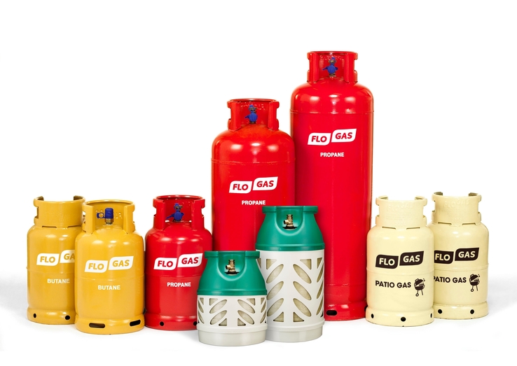 Various Flogas gas cylinders in different sizes and colors: yellow for butane, red for propane, cream for patio gas, and white and green for another type of gas. Each cylinder is labeled with the type of gas and the brand name 'Flogas.'