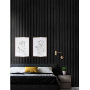 Minimalist bedroom with a dark vertical slat wall behind a black upholstered bed. The bed features white and gray bedding with a yellow accent pillow. Above are two framed line art drawings, and to the right sits a round side table with a potted plant and gold wall sconce.
